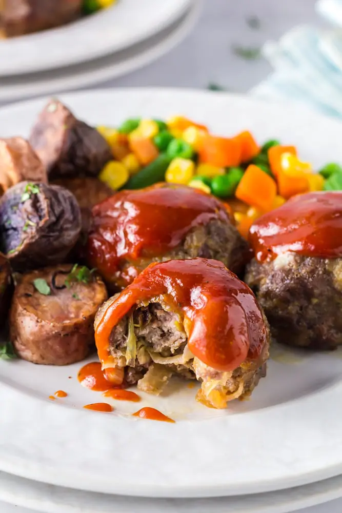 Onion Burger Mini Meatloaf covered in a bright red sauce on a white plate with a bite taken out of it