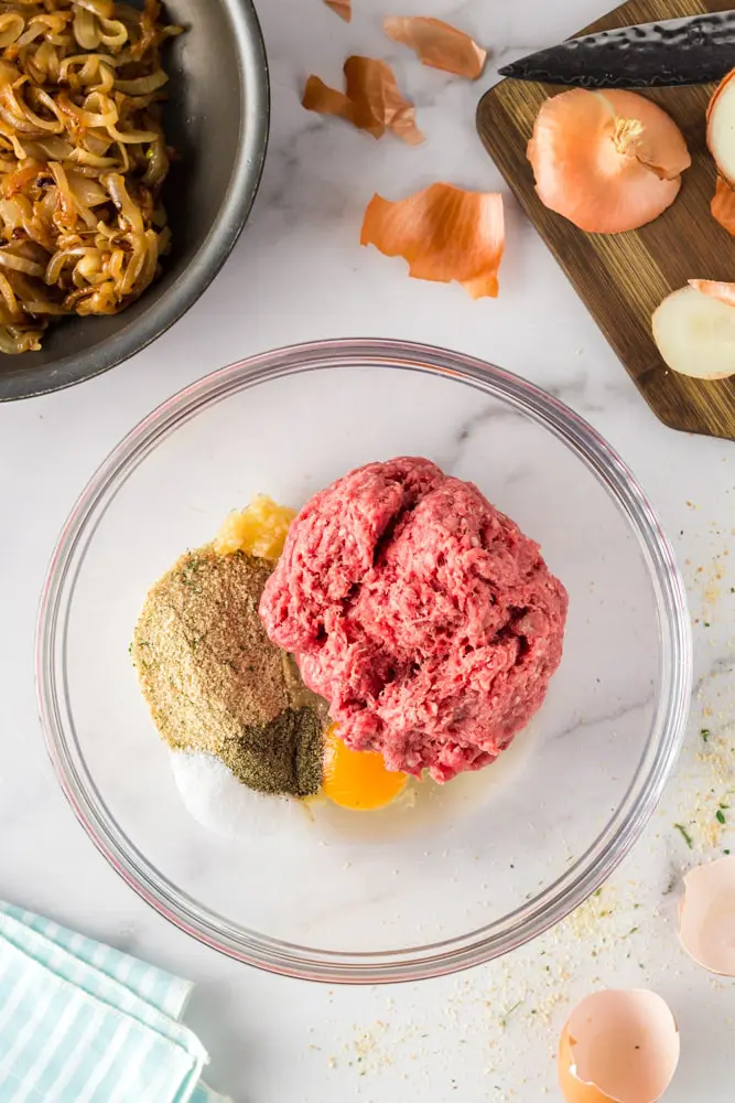 clear glass mixing bowl with meatloaf mixture ingredients expect the caramelized onions that are on the side