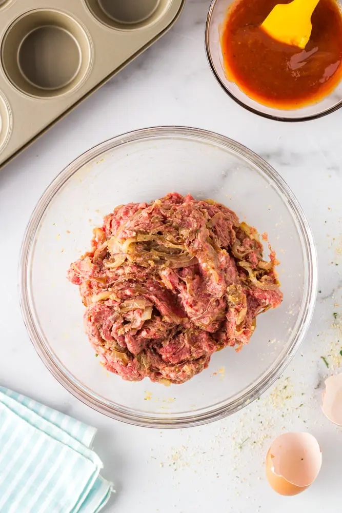 clear glass mixing bowl filled with raw onion burger meatloaf mixture