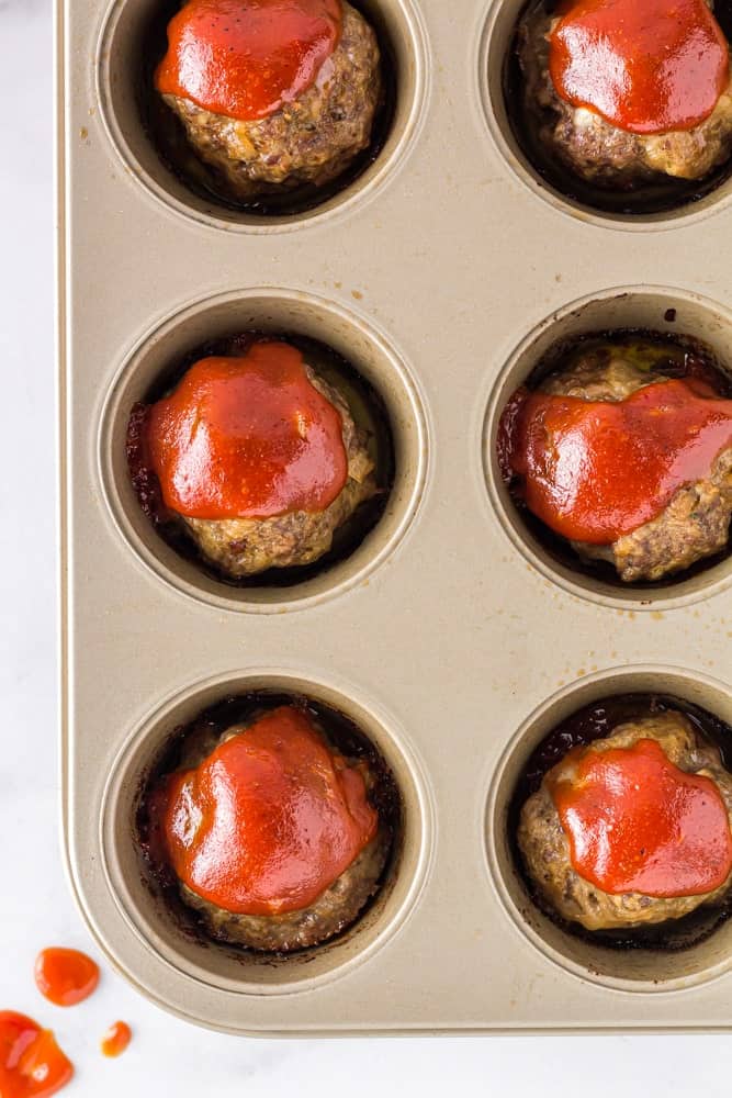 muffin pan filled with baked onion burger mini meatloaf topped with bright red sauce