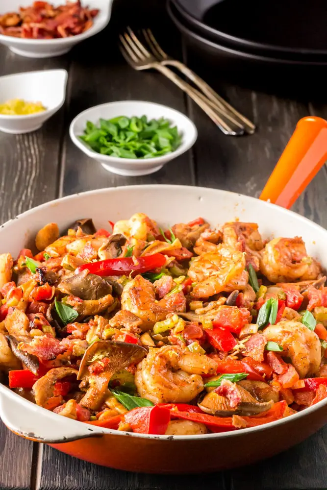 Saute pan filled with bright yellow grits, topped with shrimp smothered in a new orleans style buttery barbecue sauce and tossed with green onions, red bell peppers and mushrooms