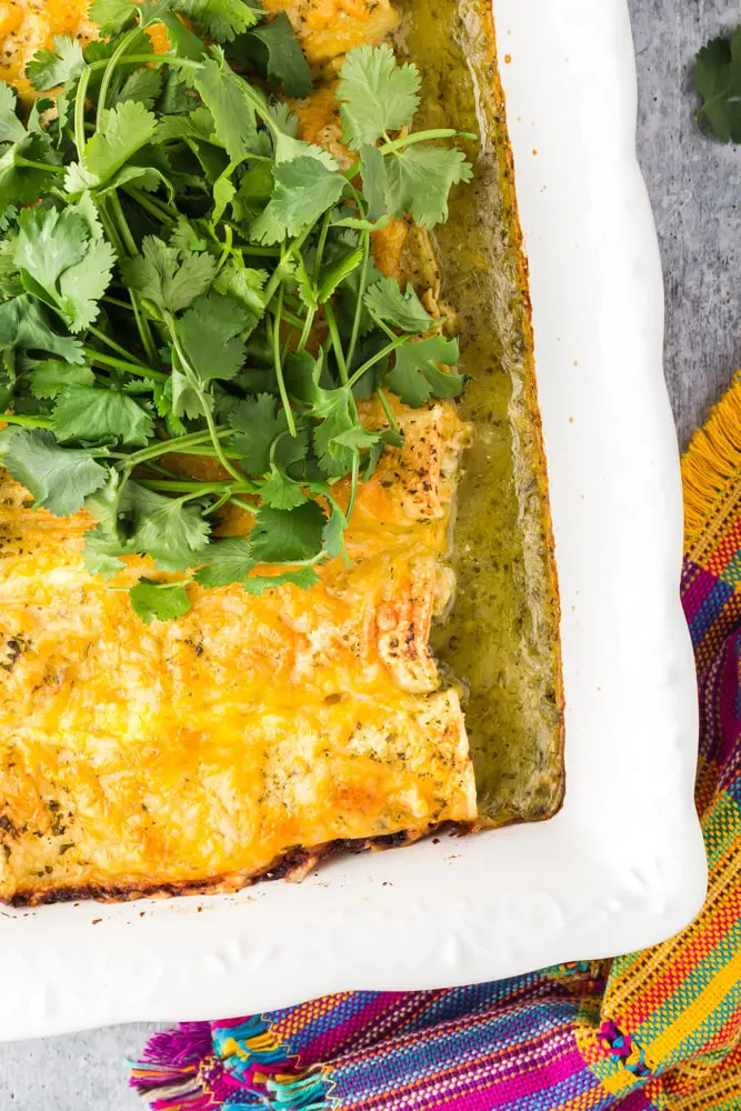 white baking dish filled with green chicken enchiladas topped with orange melted cheese and a mound of bright green cilantro