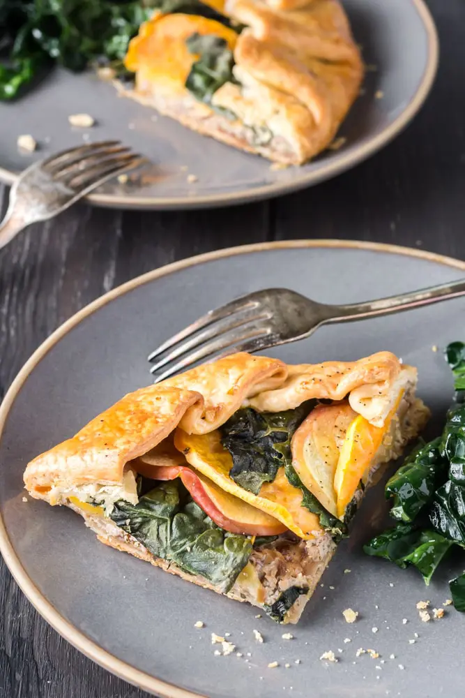 Two gray plates each with a slice of sweet potato, apple and kale galette and a small side kale salad