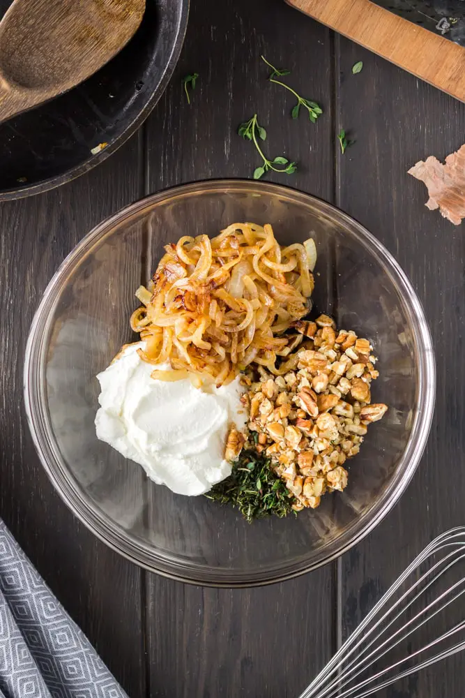 glass mixing bowl filled with white ricotta, golden caramelized onions, green chopped thyme and chopped pecans