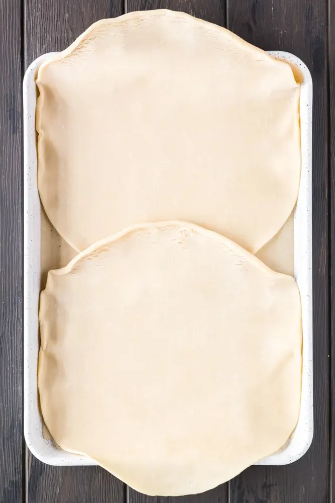 two round unbaked pie crusts on a white baking sheet line with brown parchment paper