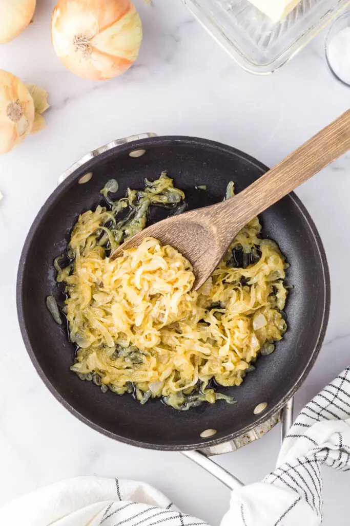 Caramelized onions being scooped from the pan with a wooden spoon