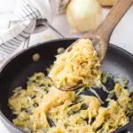Caramelized onions being scooped from the pan with a wooden spoon