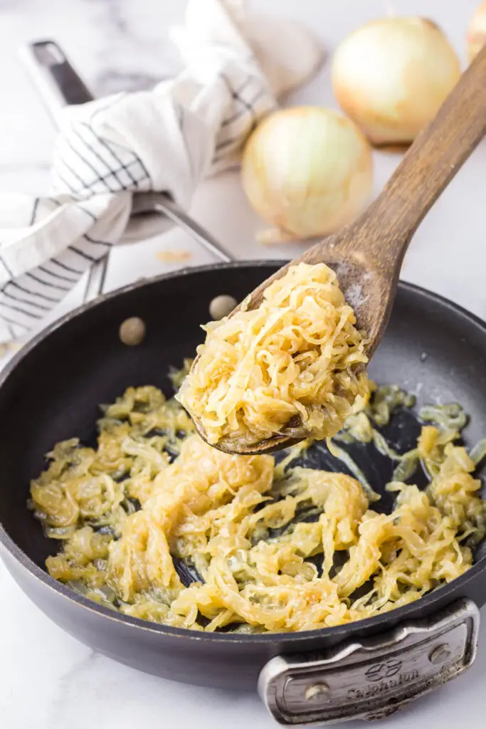 Caramelized onions being scooped from the pan with a wooden spoon