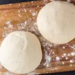 two uncooked pizza dough balls on a wooden cutting board