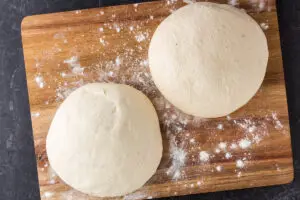 two uncooked pizza dough balls on a wooden cutting board