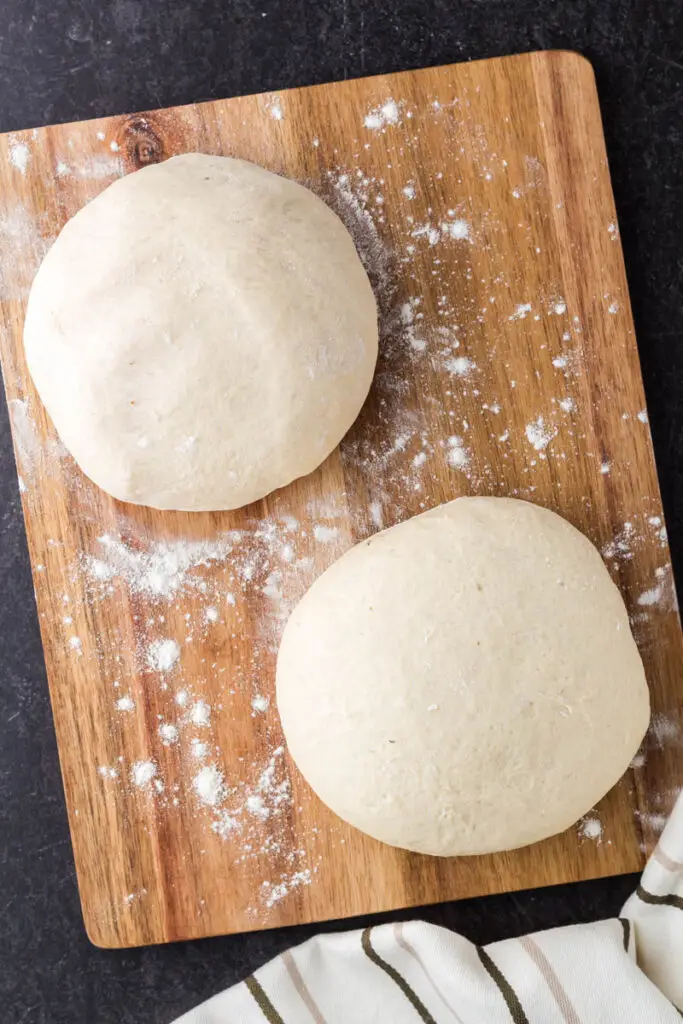 two uncooked pizza dough balls on a wooden cutting board