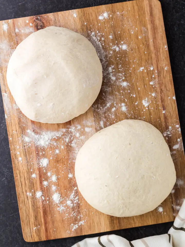 two uncooked pizza dough balls on a wooden cutting board