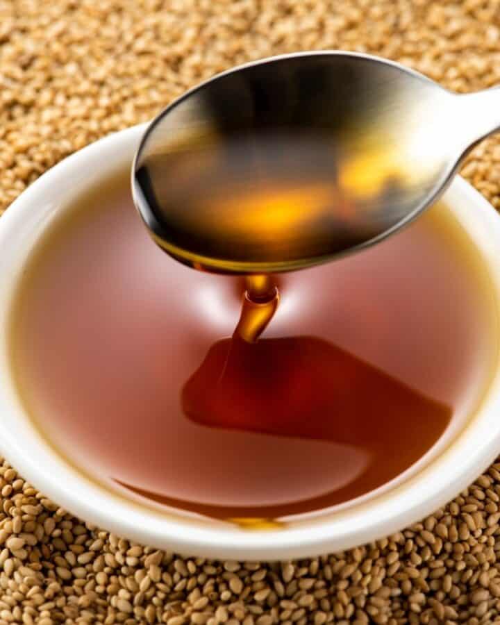 small bowl of sesame oil with spoon sitting on top of toasted sesame seeds.