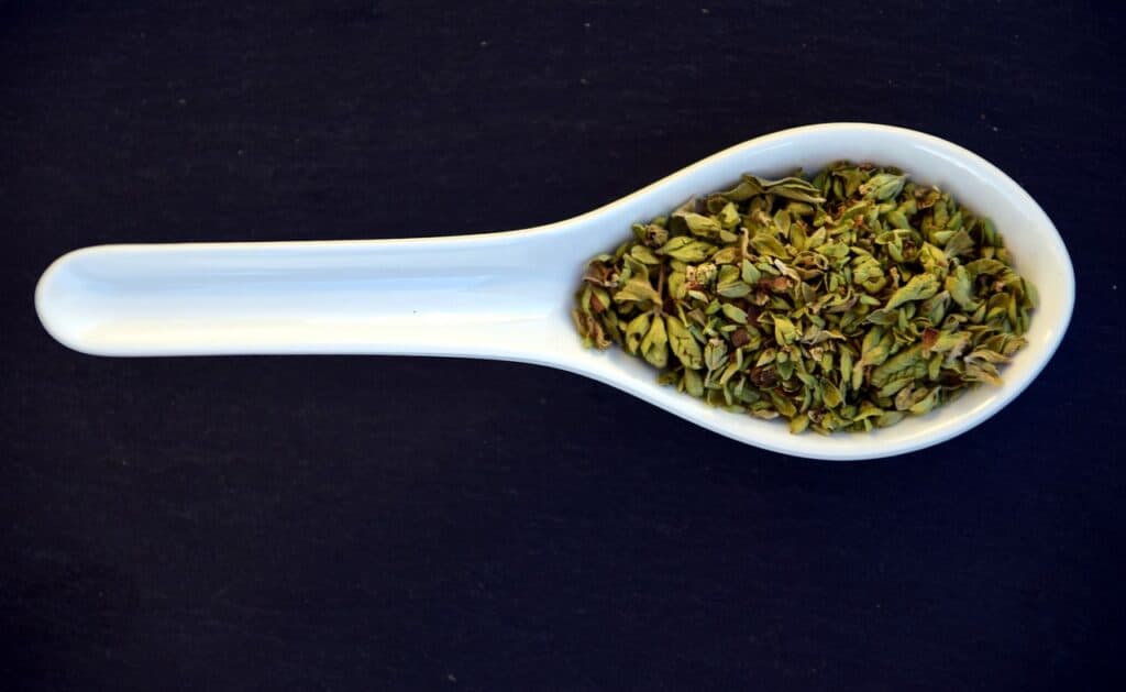 white spoon filled with dried herb leaves