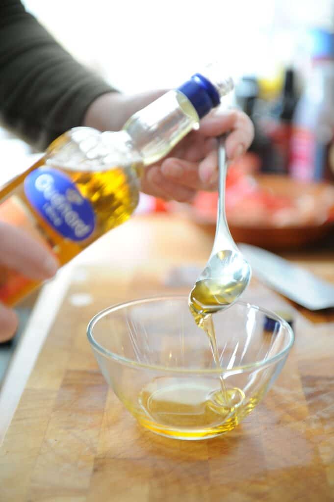 walnut oil being poured from a spoon into a small glass bowl.