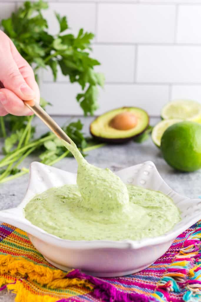 spoonful of creamy avocado sauce being spooned from a white bowl.