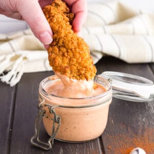 chicken strip being dipped into glass jar of cane's sauce.