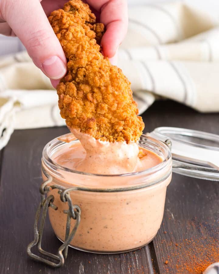 chicken strip being dipped into glass jar of cane's sauce.