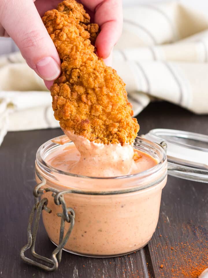 chicken strip being dipped into glass jar of cane's sauce.