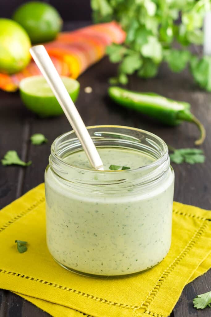 Glass jar filled with light green Cilantro Lime Sauce with Garlic sauce on a yellow napkin.