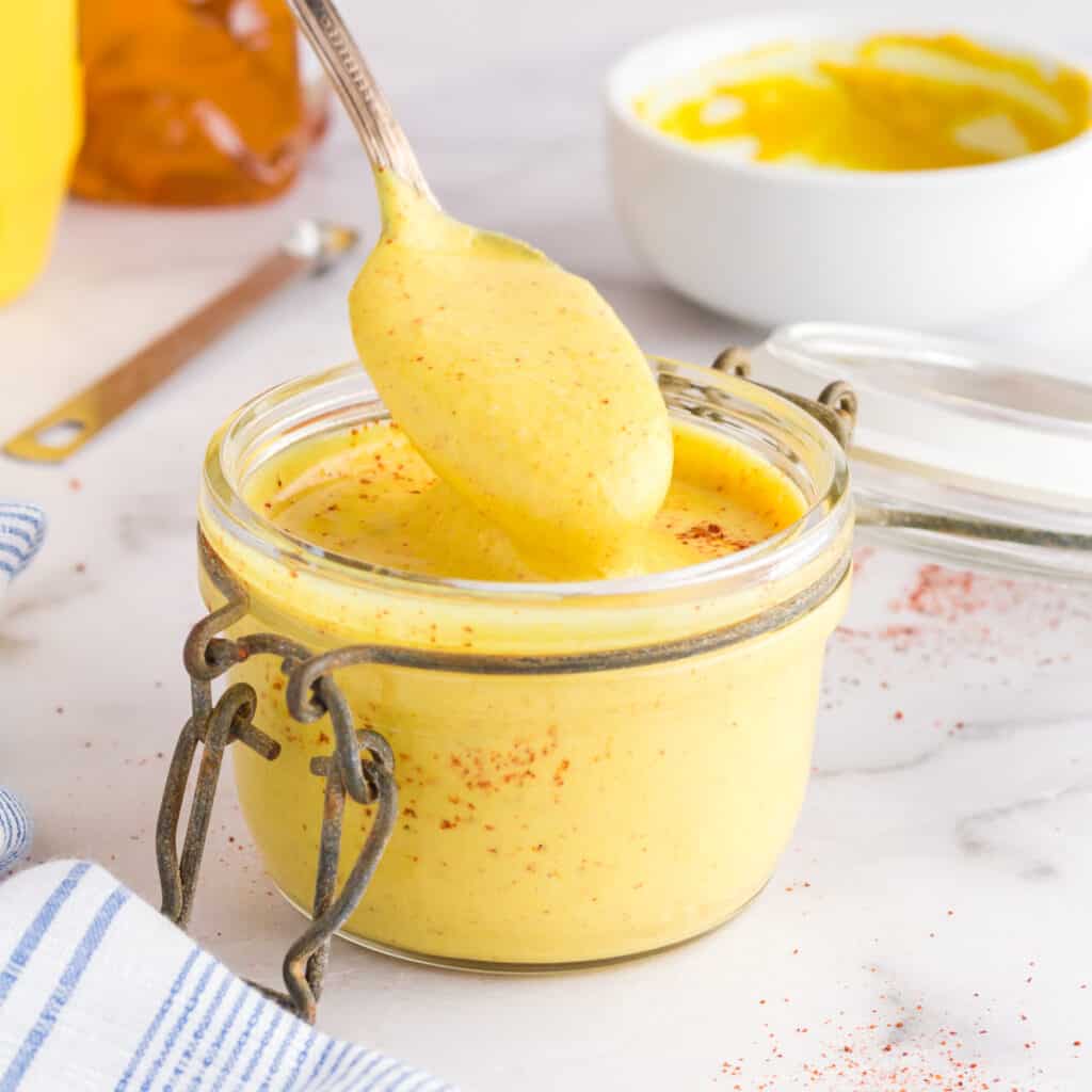 Bright yellow honey mustard dressing with flecks of red cayenne pepper in a small glass jar.