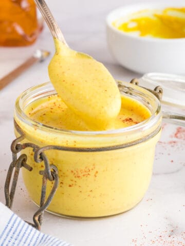Bright yellow honey mustard dressing with flecks of red cayenne pepper in a small glass jar.