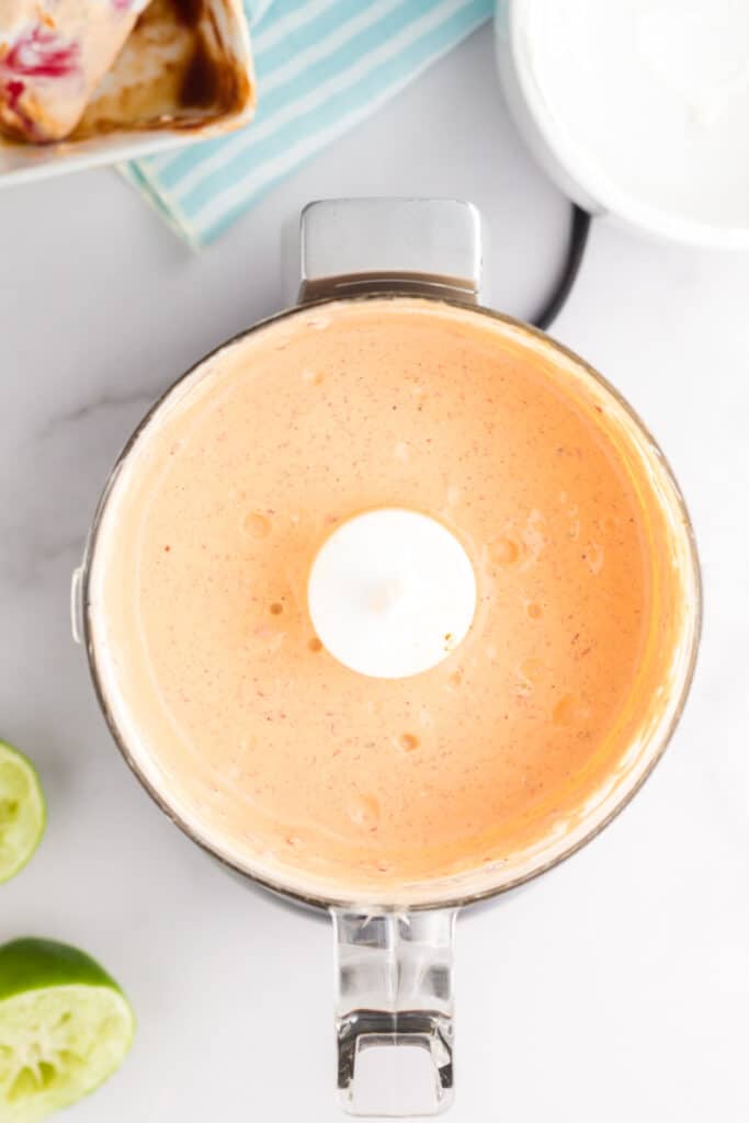 Small food processor filled with orange chipotle sour cream sauce for tacos.