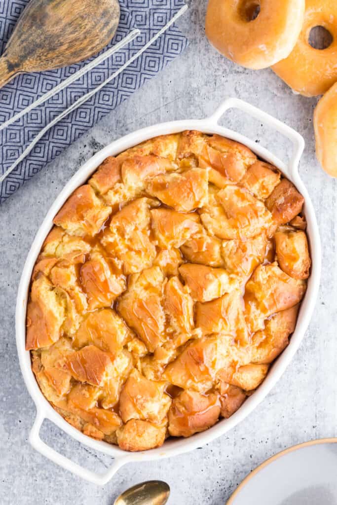 Oval pan filled with donut bread pudding fresh from the oven drizzled with caramel sauce.