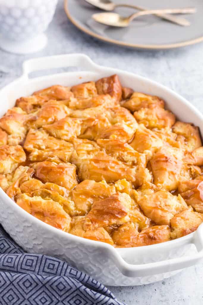 Oval pan filled with donut bread pudding fresh from the oven drizzled with caramel sauce.