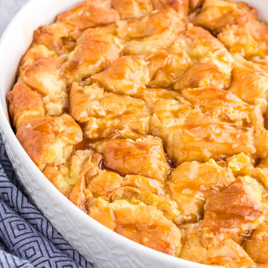 Oval pan filled with donut bread pudding fresh from the oven drizzled with caramel sauce.