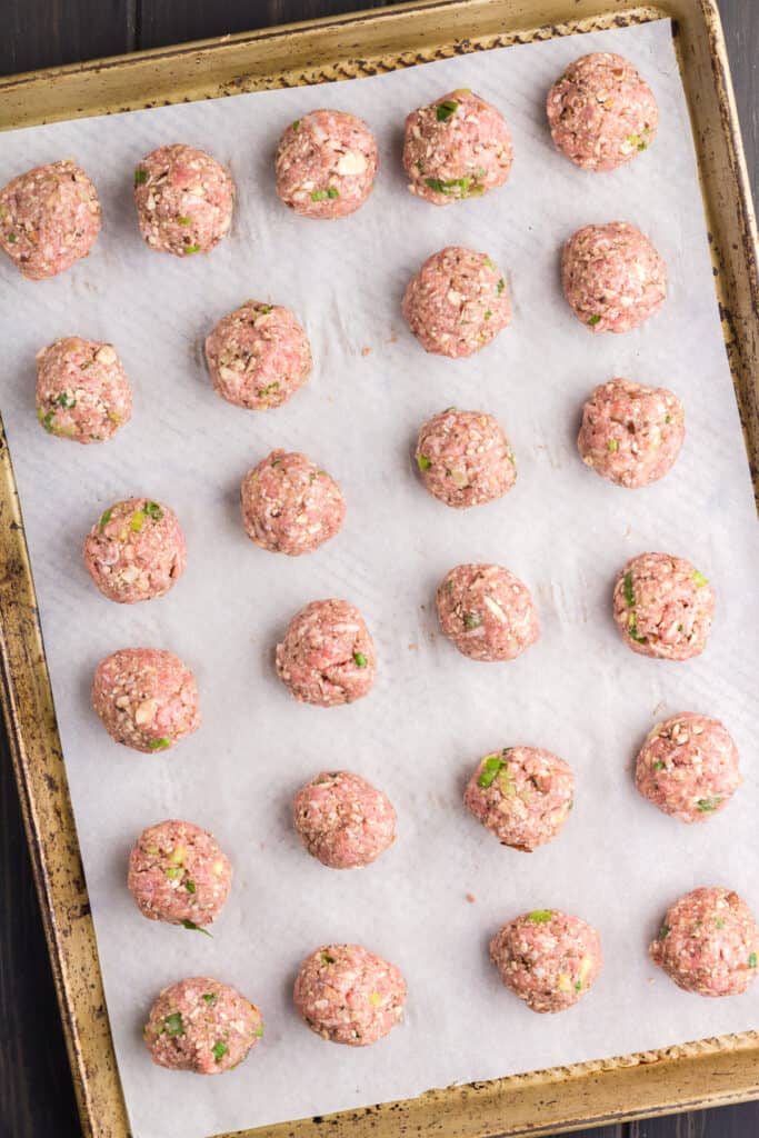 Sheet pan topped with parchment paper and uncooked meatballs before going into the oven.