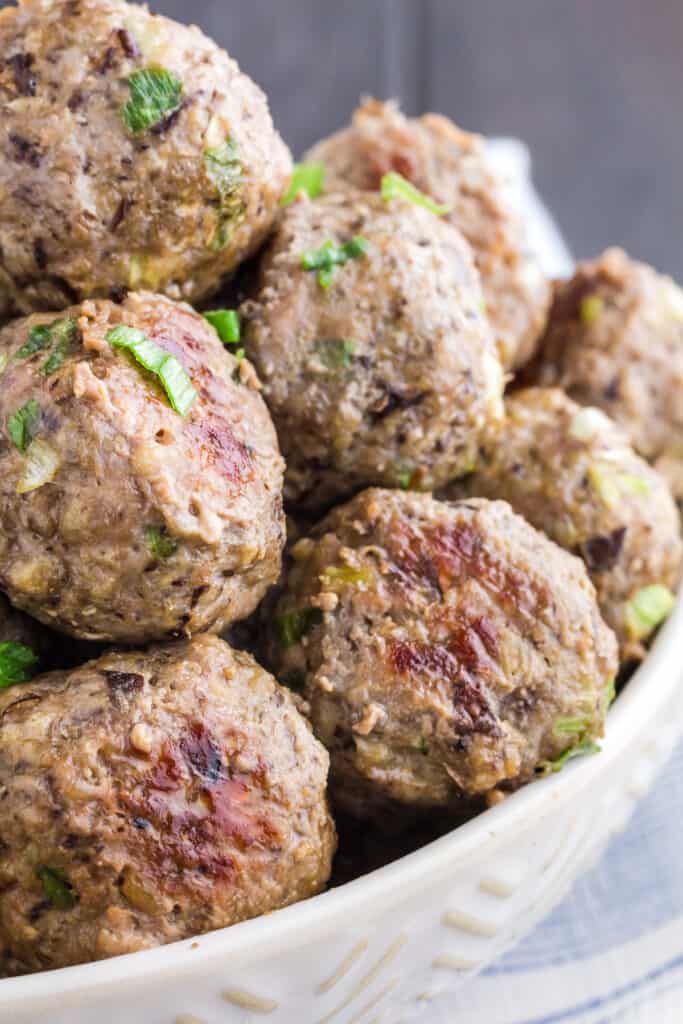 Close up of white bowl filled with brown meatballs sprinkled with green onions.