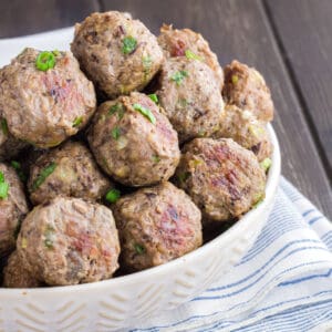 Close up of white bowl filled with brown meatballs sprinkled with green onions.