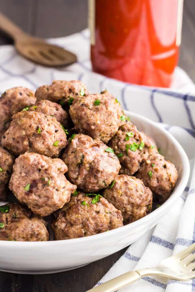 Pile of mini meatballs sprinkled with green parsley served in a white bowl.