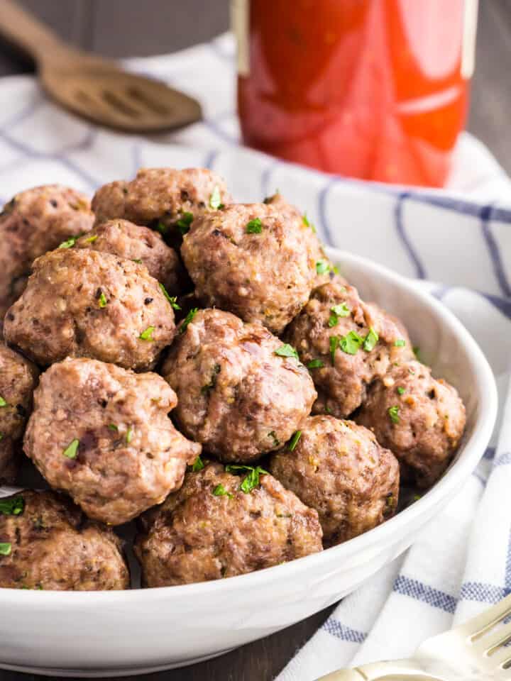 Pile of mini meatballs sprinkled with green parsley served in a white bowl.