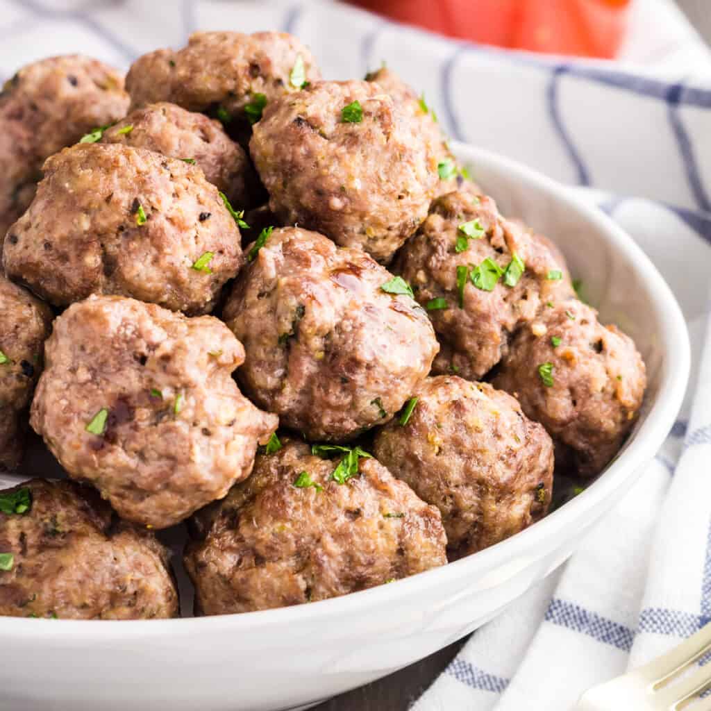 Pile of mini meatballs sprinkled with green parsley served in a white bowl.