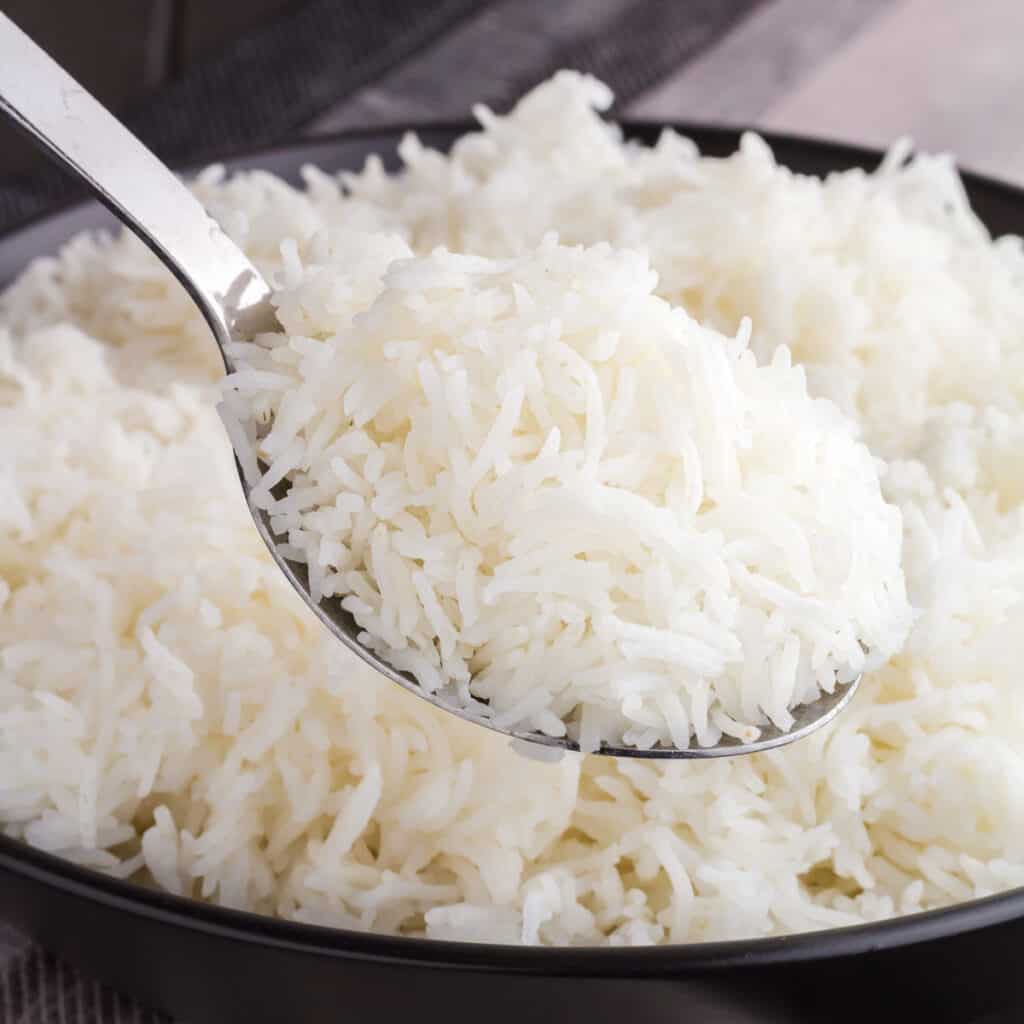 Silver spoon scooping white rice from a black bowl.