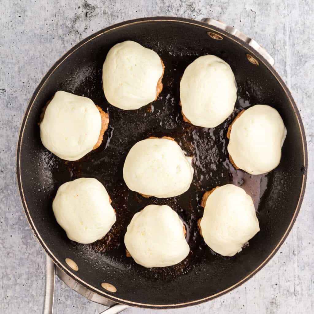 Pizza Burger Slider patties covered in soppressata and mozzarella in a black skillet.