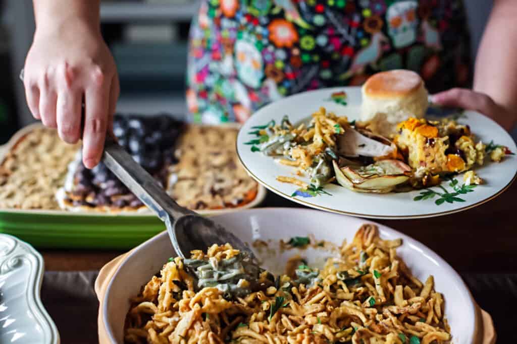 green bean casserole being served on to a plate with other Thanksgiving dishes