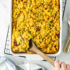 Traditional Southern Cornbread Dressing being scooped out of a white baking dish with a wooden sppon.