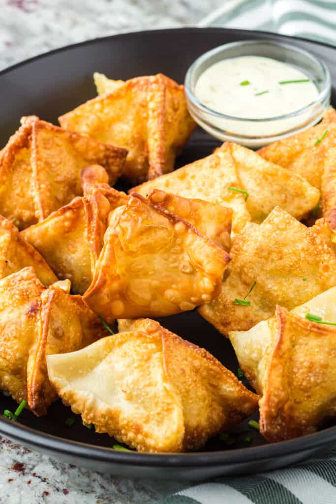 A black plate of jalapeno popper wontons with a side of ranch.