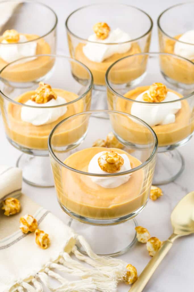 6 mini trifle glasses filled with homemade salted caramel pudding topped with whipped cream and a piece of caramel corn.