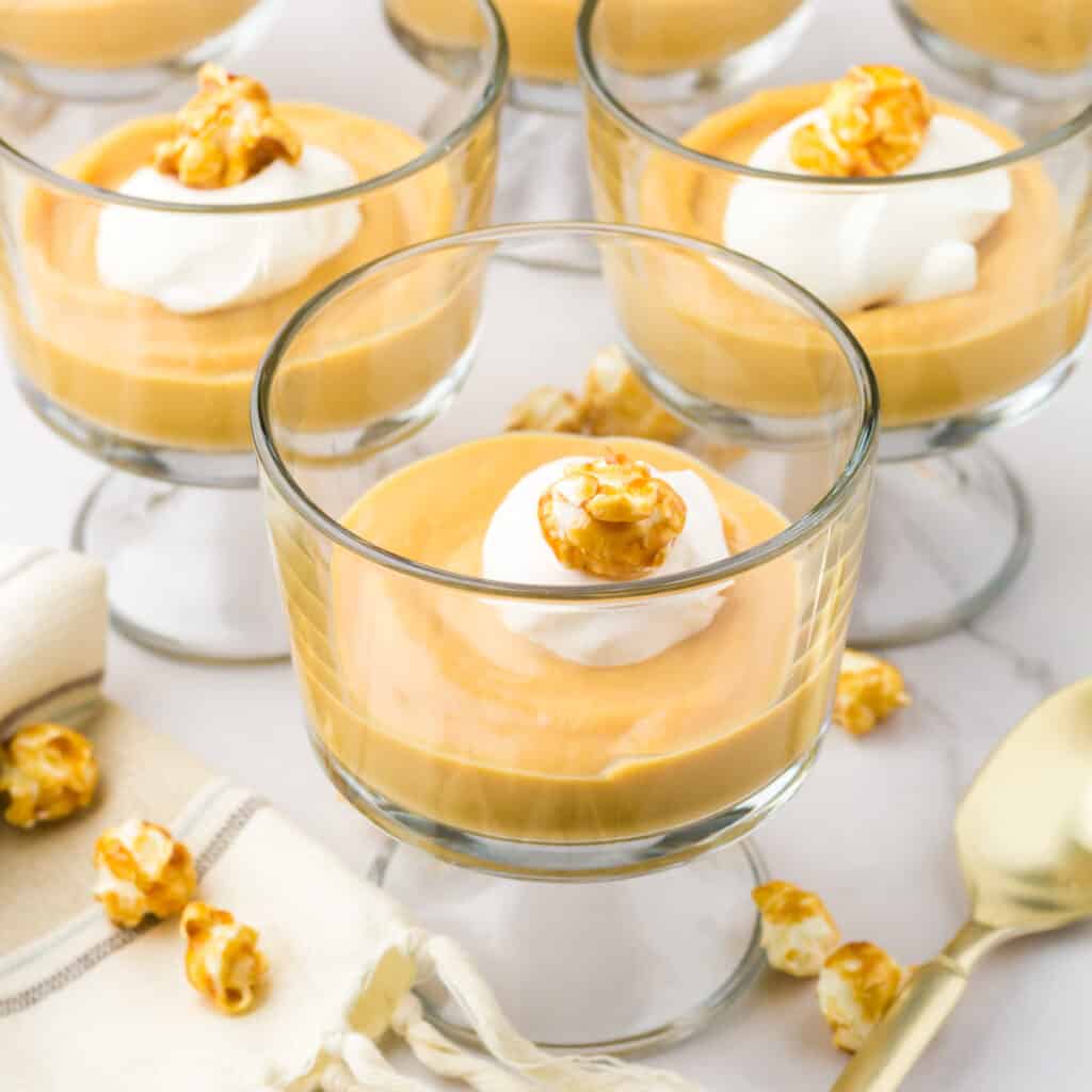 Homemade salted caramel pudding topped with whipped cream and a piece of caramel corn in a mini glass trifle glass.