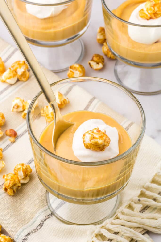 Homemade salted caramel pudding topped with whipped cream and a piece of caramel corn in a mini glass trifle glass.