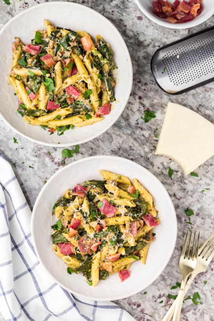 Two white bowls filled with bacon pesto pasta.