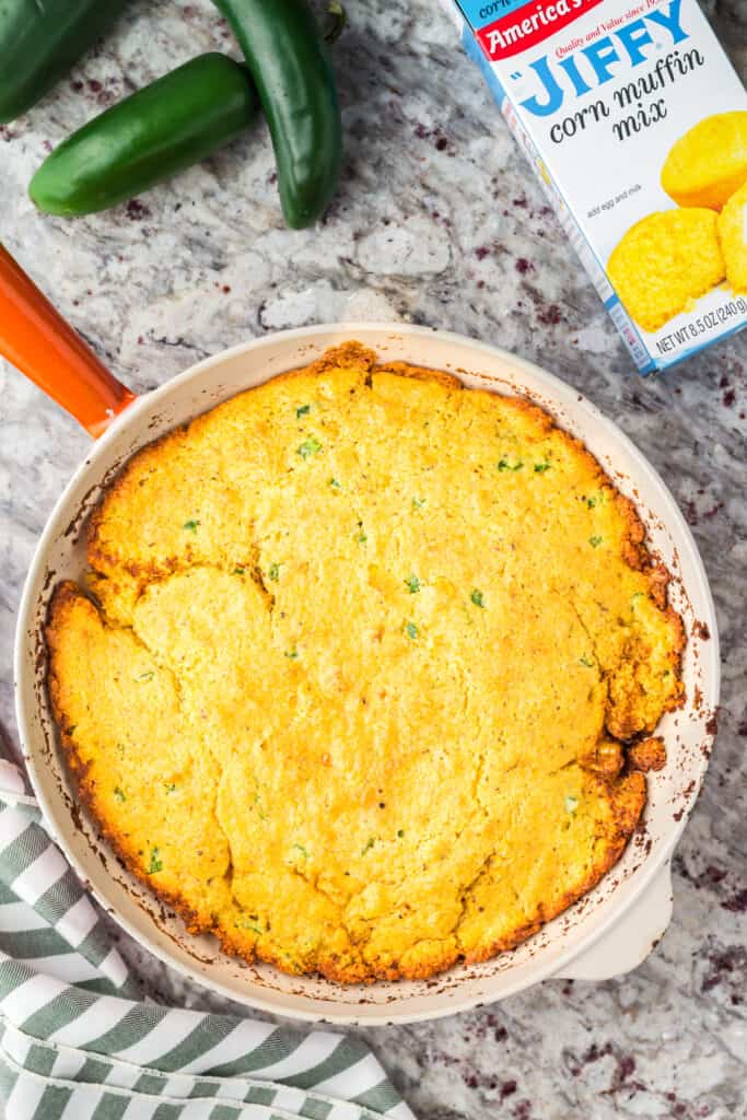 Skillet of Jiffy Jalapeño Cornbread with an empty box of Jiffy corn muffin mix on the side.