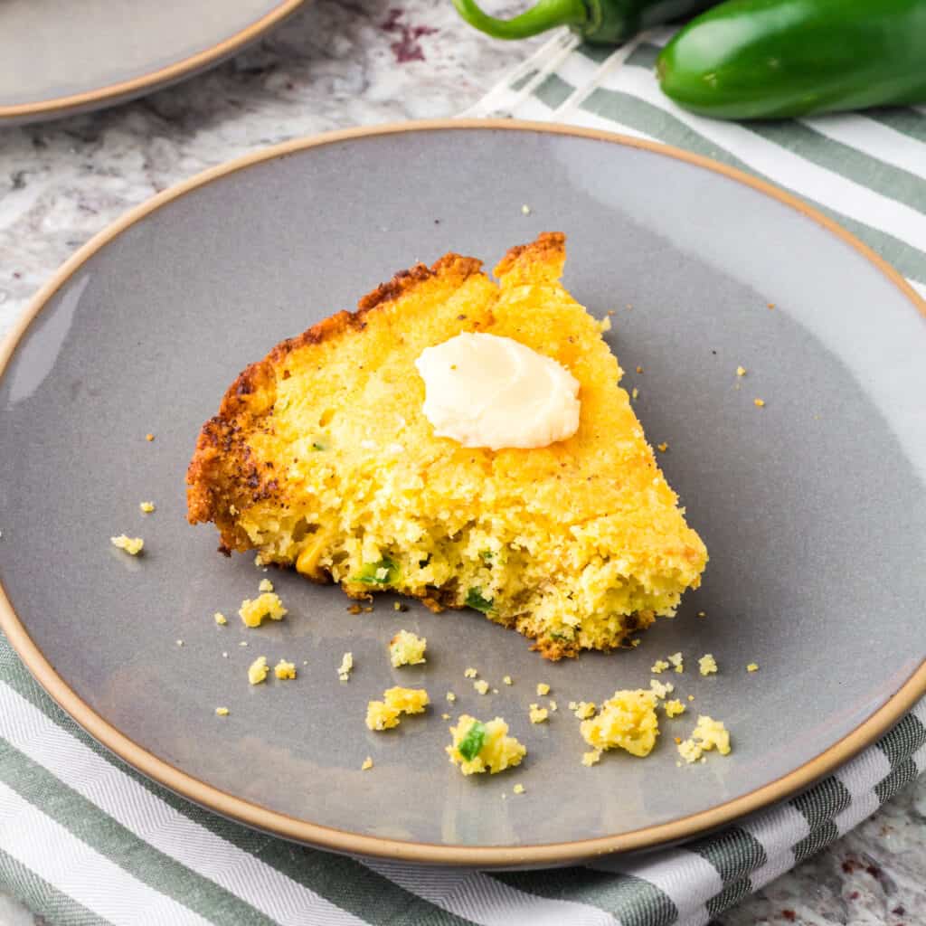 A slice of Jiffy Jalapeño Cornbread on a grey plate with a green and white striped napkin.