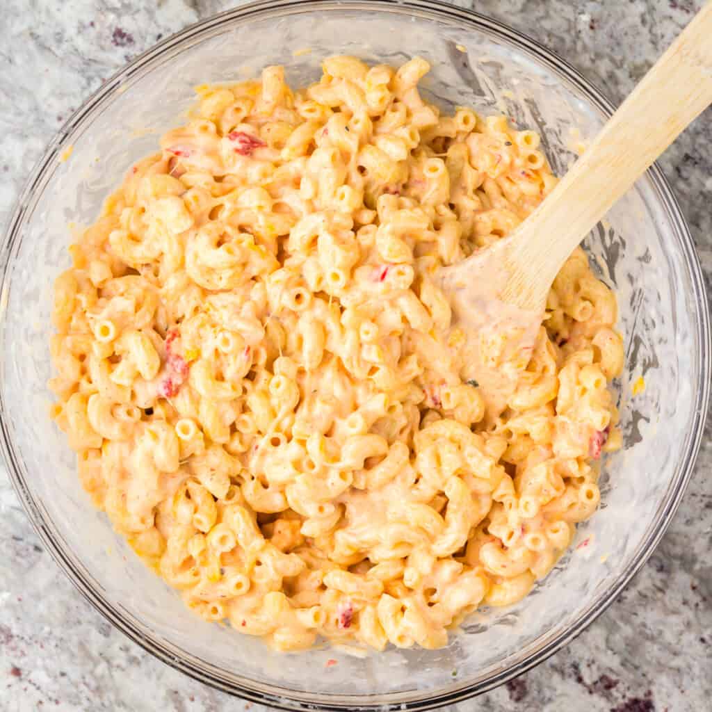 Noodles combined with white sauce, pimento cheese, and shredded cheese in a large glass bowl.