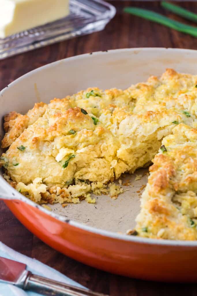 Skillet biscuit in an orange pan with a piece removed.